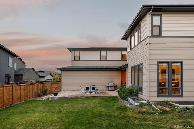 back house at dusk featuring a yard and a patio