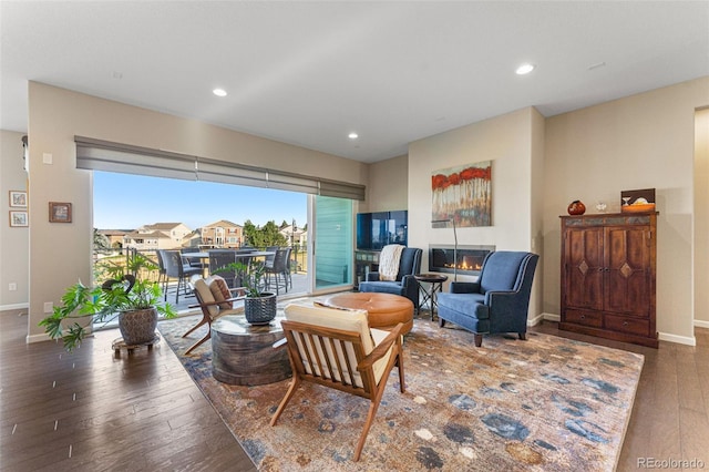 living room featuring a glass covered fireplace, baseboards, recessed lighting, and wood finished floors