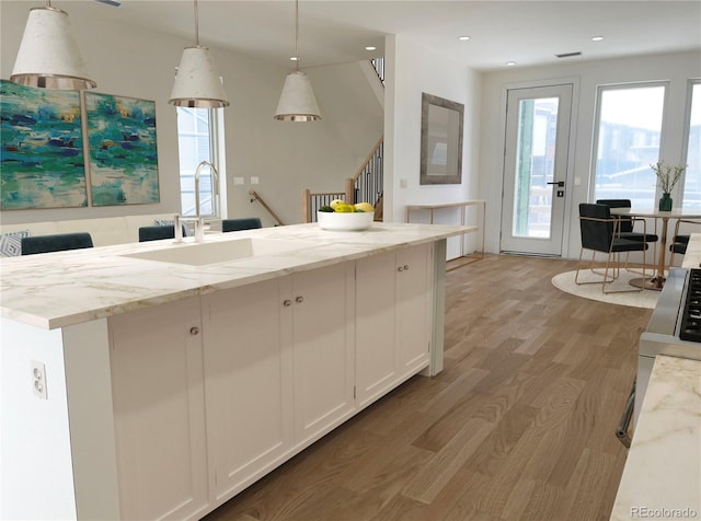 kitchen featuring white cabinetry, light stone countertops, sink, decorative light fixtures, and hardwood / wood-style flooring