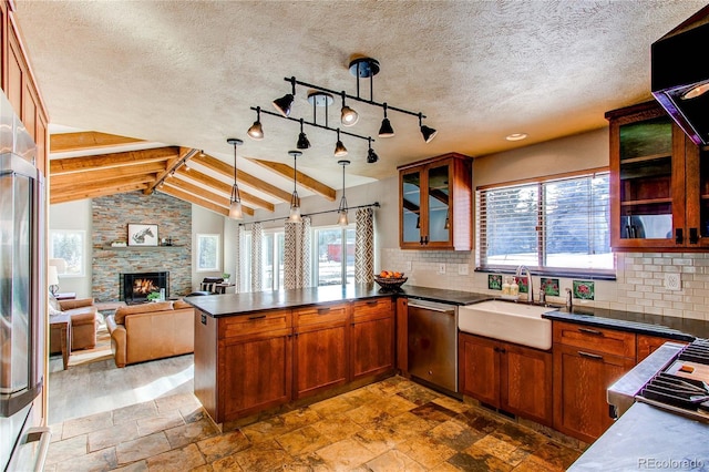 kitchen with dishwasher, sink, vaulted ceiling with beams, a stone fireplace, and decorative light fixtures