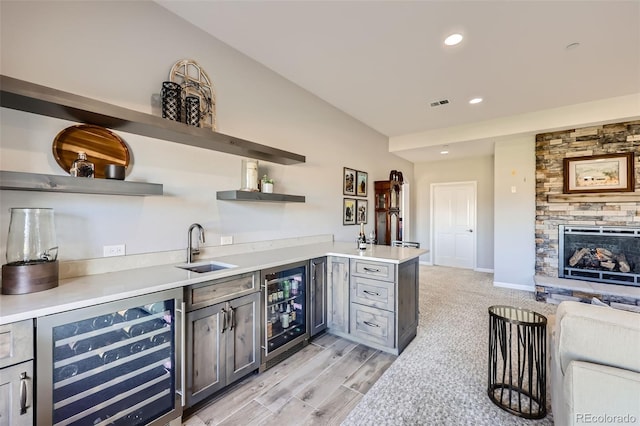 indoor wet bar with wine cooler, a stone fireplace, recessed lighting, light wood-style floors, and baseboards