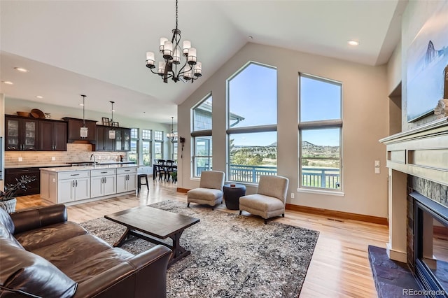 living area with a chandelier, light wood-type flooring, a fireplace with flush hearth, baseboards, and high vaulted ceiling