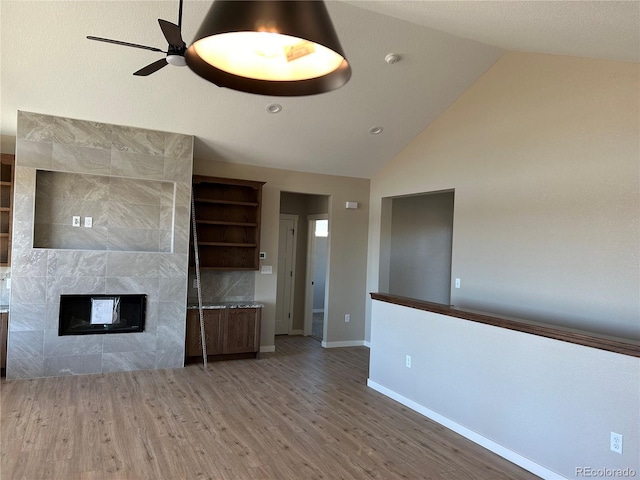 unfurnished living room with ceiling fan, wood-type flooring, high vaulted ceiling, and a tile fireplace