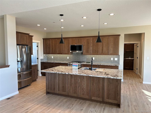 kitchen with appliances with stainless steel finishes, decorative light fixtures, light stone countertops, and a center island with sink