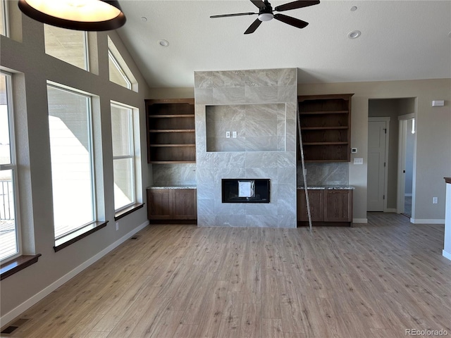 unfurnished living room featuring built in shelves, lofted ceiling, ceiling fan, a tiled fireplace, and light hardwood / wood-style floors