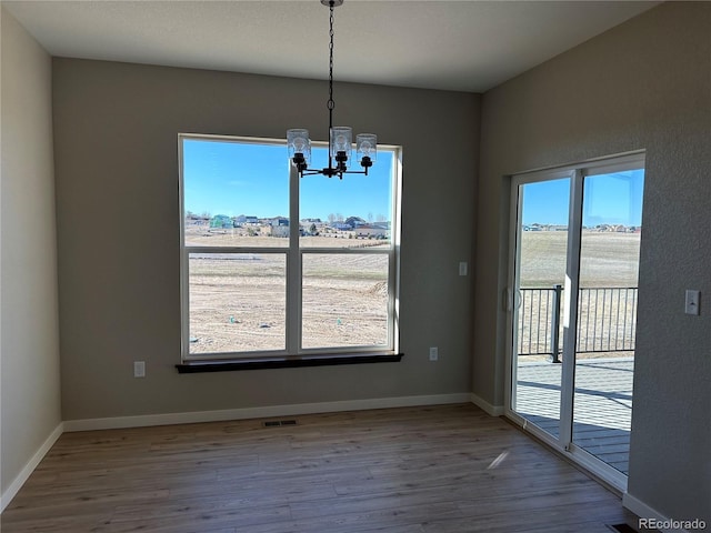 unfurnished dining area with a notable chandelier, wood-type flooring, and a wealth of natural light