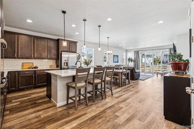 kitchen with recessed lighting, dark brown cabinetry, stainless steel refrigerator with ice dispenser, wood finished floors, and light countertops