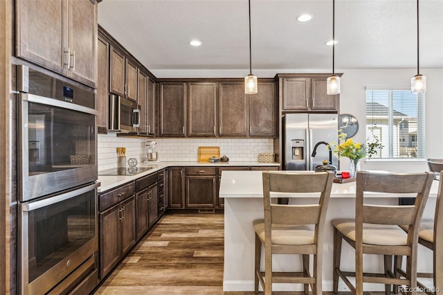 kitchen with dark brown cabinets, stainless steel appliances, decorative backsplash, and wood finished floors