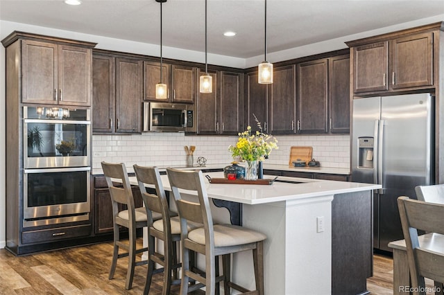 kitchen featuring dark brown cabinets, dark wood-style flooring, backsplash, a center island with sink, and appliances with stainless steel finishes
