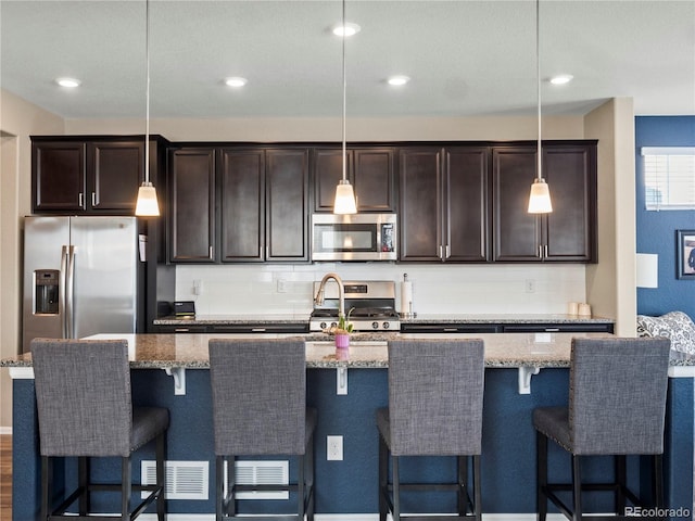 kitchen with hanging light fixtures, decorative backsplash, a center island with sink, and appliances with stainless steel finishes