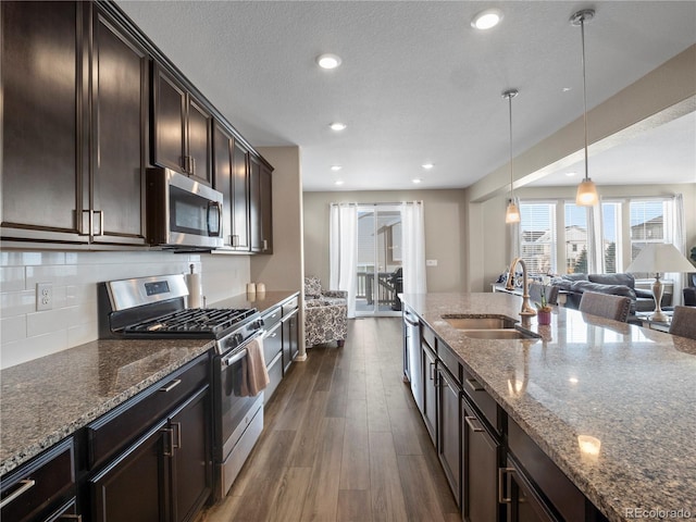 kitchen with appliances with stainless steel finishes, pendant lighting, sink, dark stone countertops, and dark brown cabinetry