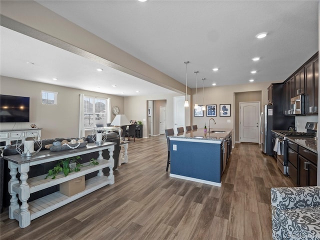 kitchen featuring sink, stainless steel appliances, dark brown cabinetry, a center island with sink, and dark stone counters