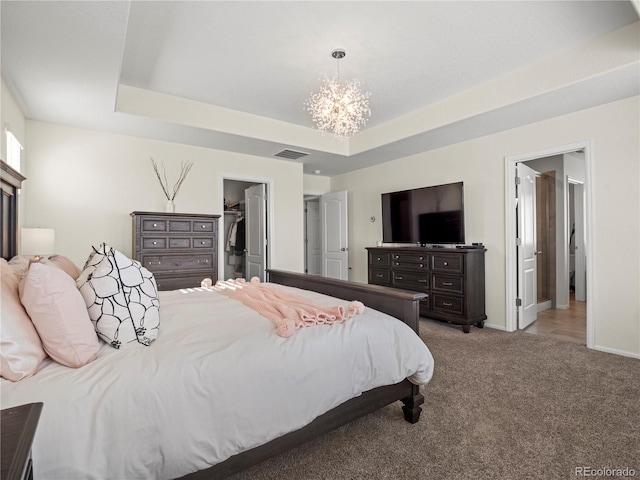 carpeted bedroom with an inviting chandelier, a walk in closet, a raised ceiling, and a closet