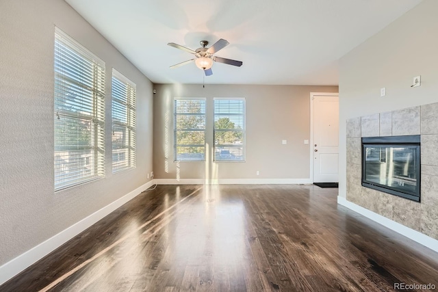 unfurnished living room with ceiling fan, a tiled fireplace, and dark wood-type flooring