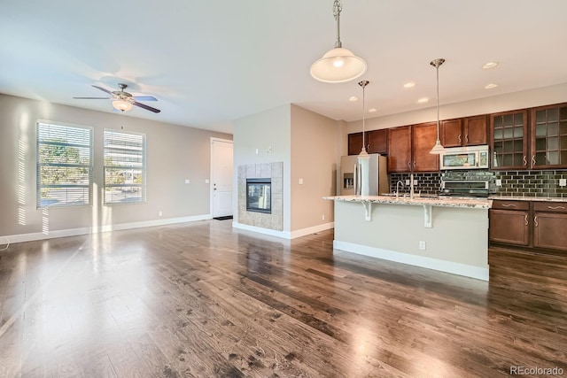 kitchen with a breakfast bar area, dark hardwood / wood-style flooring, pendant lighting, stainless steel appliances, and a kitchen island with sink