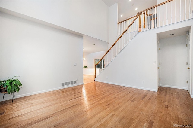5607 S Gray St, Littleton, CO 80123 - unfurnished living room with visible vents, light wood-style flooring, stairs, and a towering ceiling