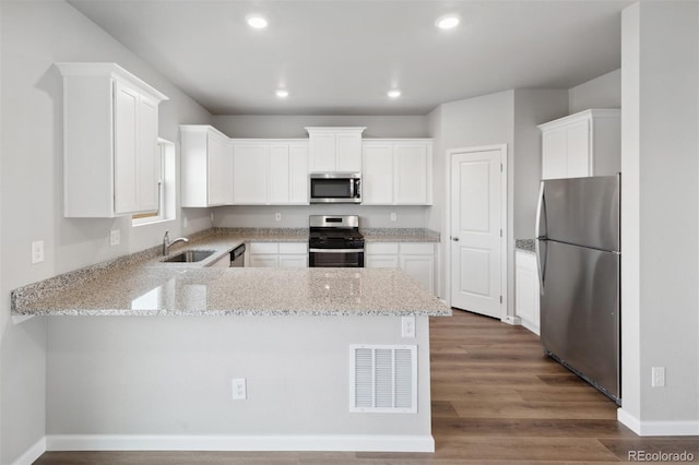 kitchen featuring visible vents, appliances with stainless steel finishes, wood finished floors, a peninsula, and a sink