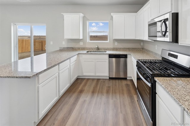 kitchen with white cabinets, appliances with stainless steel finishes, a peninsula, light wood-style floors, and a sink