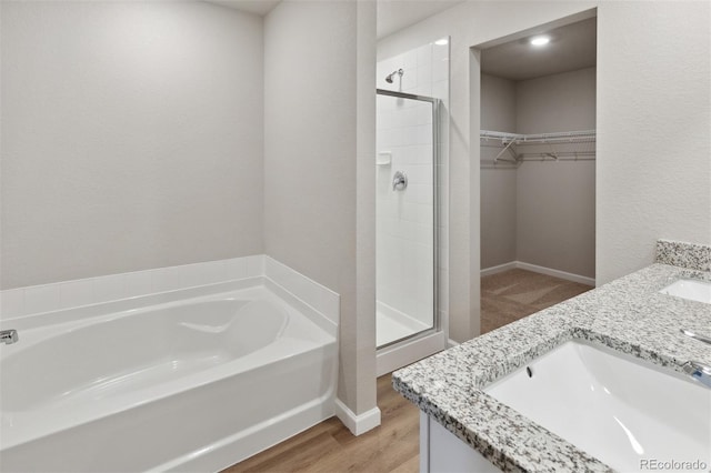 bathroom featuring a garden tub, wood finished floors, a sink, a spacious closet, and a shower stall