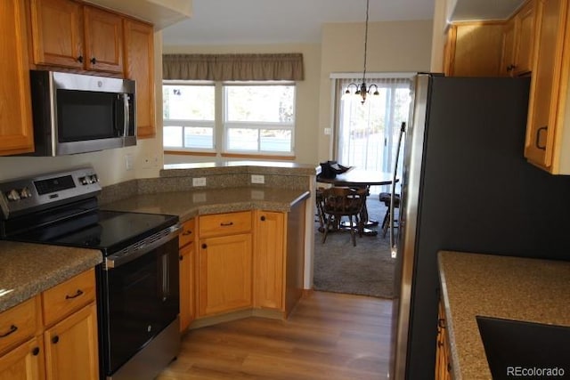 kitchen featuring pendant lighting, stainless steel appliances, stone countertops, a chandelier, and light wood-type flooring