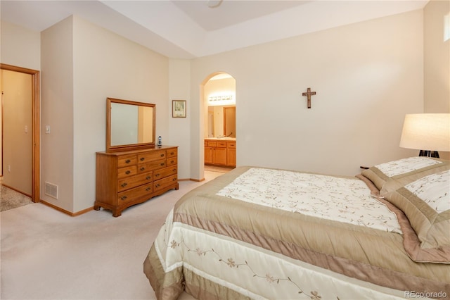 bedroom with ensuite bathroom and light carpet