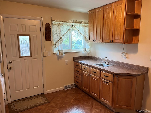 kitchen with dark countertops, visible vents, brown cabinetry, and a sink