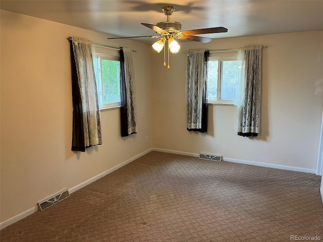 carpeted empty room with a healthy amount of sunlight, a ceiling fan, and visible vents
