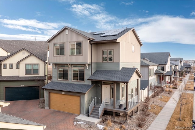 view of front of property with covered porch, a residential view, decorative driveway, roof mounted solar panels, and an attached garage