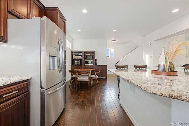 kitchen featuring light stone countertops, a kitchen breakfast bar, dark wood-type flooring, recessed lighting, and stainless steel fridge with ice dispenser
