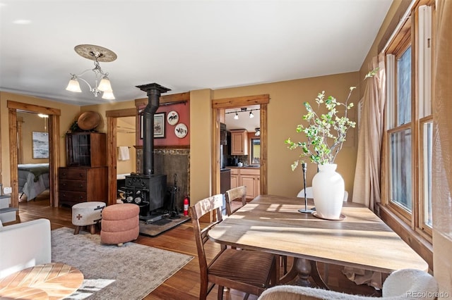 dining space featuring hardwood / wood-style flooring, plenty of natural light, a chandelier, and a wood stove