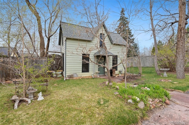view of front facade featuring a shingled roof, fence, and a front lawn
