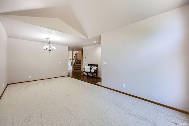 unfurnished room featuring dark carpet, lofted ceiling, and a notable chandelier