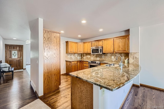 kitchen with appliances with stainless steel finishes, backsplash, light stone counters, sink, and hardwood / wood-style flooring