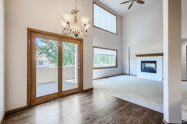 unfurnished living room with ceiling fan with notable chandelier, a fireplace, a wealth of natural light, and a high ceiling