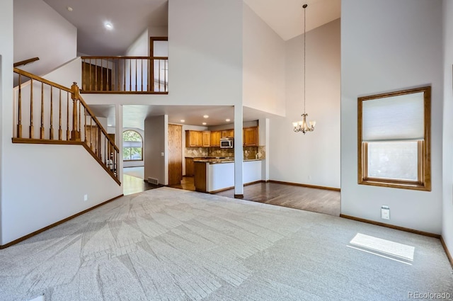 unfurnished living room with light carpet, an inviting chandelier, and high vaulted ceiling