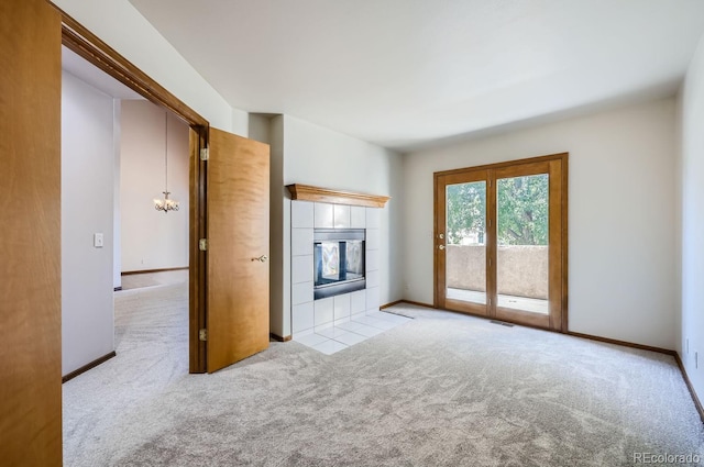 unfurnished living room featuring a tiled fireplace, light colored carpet, and an inviting chandelier