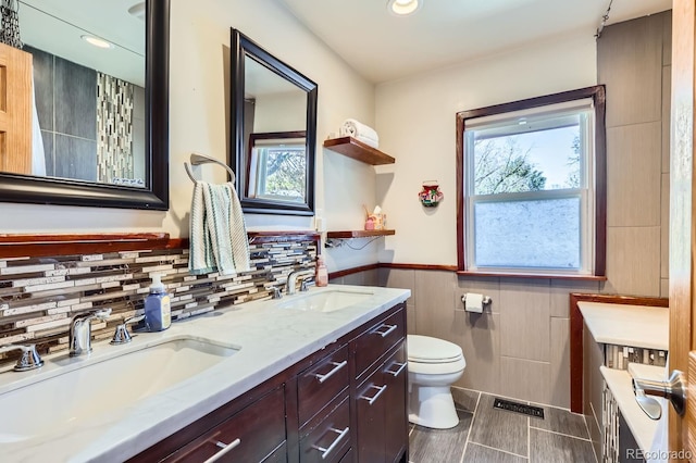 bathroom with vanity, toilet, and tile walls