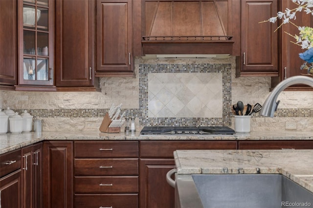 kitchen featuring decorative backsplash, glass insert cabinets, custom exhaust hood, and stainless steel gas stovetop