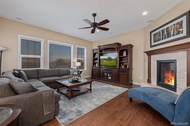 living area with ceiling fan, wood finished floors, baseboards, a warm lit fireplace, and recessed lighting