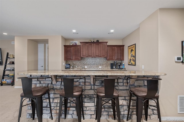 kitchen with a breakfast bar, light stone counters, recessed lighting, baseboards, and decorative backsplash