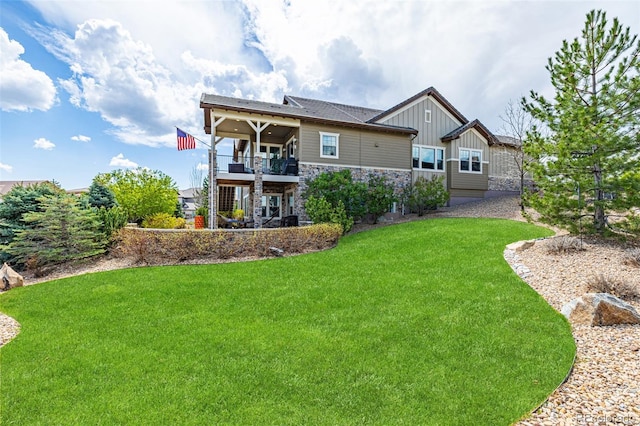 back of property with a yard, board and batten siding, a balcony, and stone siding
