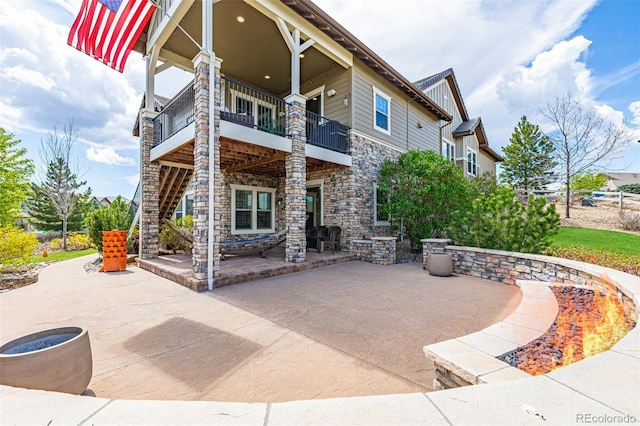 back of property with stone siding, a patio area, and a balcony