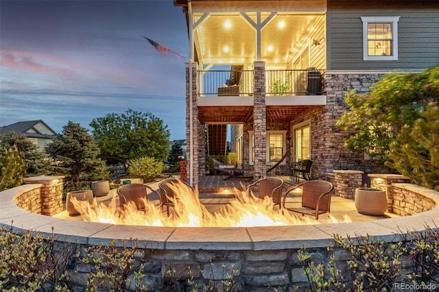 back of house with stone siding, an outdoor fire pit, and a balcony