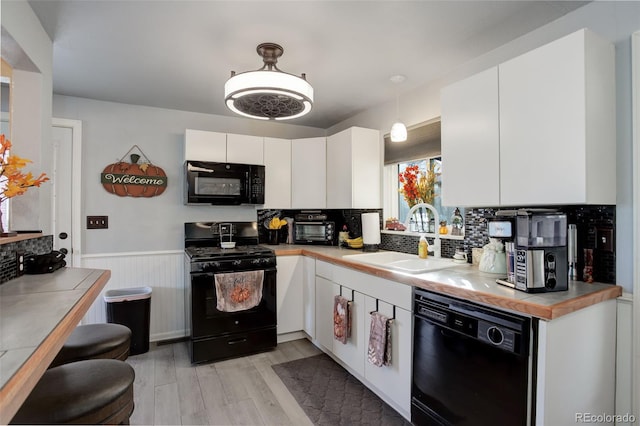 kitchen with white cabinetry, light wood-type flooring, hanging light fixtures, black appliances, and sink