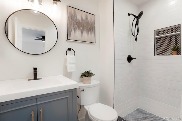 bathroom featuring a ceiling fan, toilet, vanity, and a tile shower