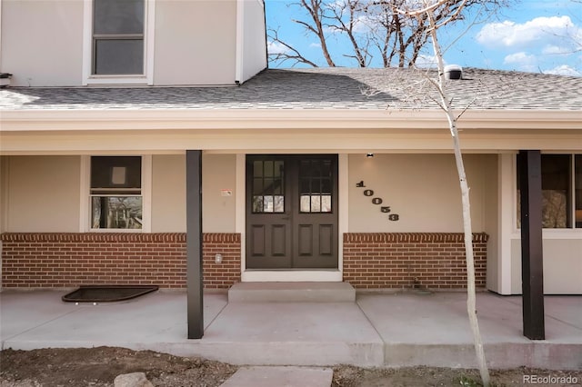 view of exterior entry featuring brick siding, a porch, and a shingled roof