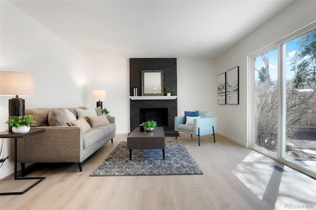 living area with a brick fireplace, baseboards, and light wood-type flooring