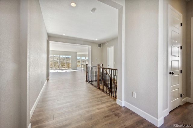 hall with an upstairs landing, wood finished floors, visible vents, and baseboards