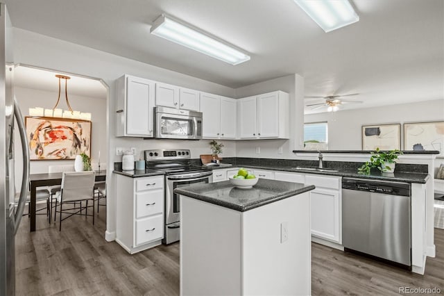 kitchen featuring stainless steel appliances, a peninsula, wood finished floors, a sink, and white cabinetry