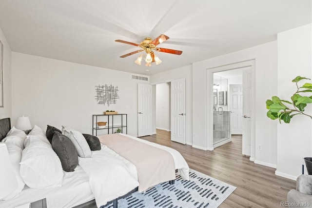 bedroom featuring wood finished floors, a ceiling fan, visible vents, baseboards, and ensuite bath